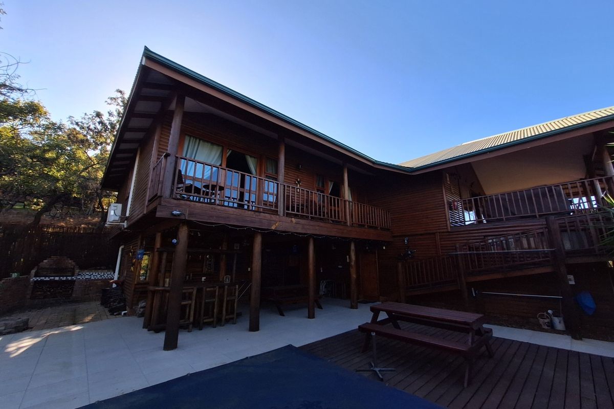Rear view of a multi-level timber house featuring a spacious covered patio, wooden balcony, and built-in brick braai area.