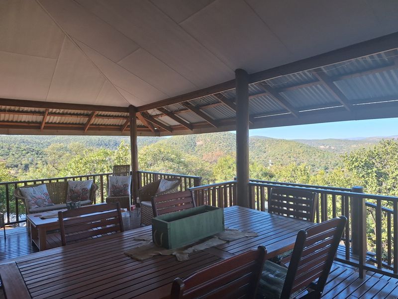 Spacious covered outdoor patio featuring timber decking, wooden balustrades, and panoramic views of the surrounding hills and landscape.