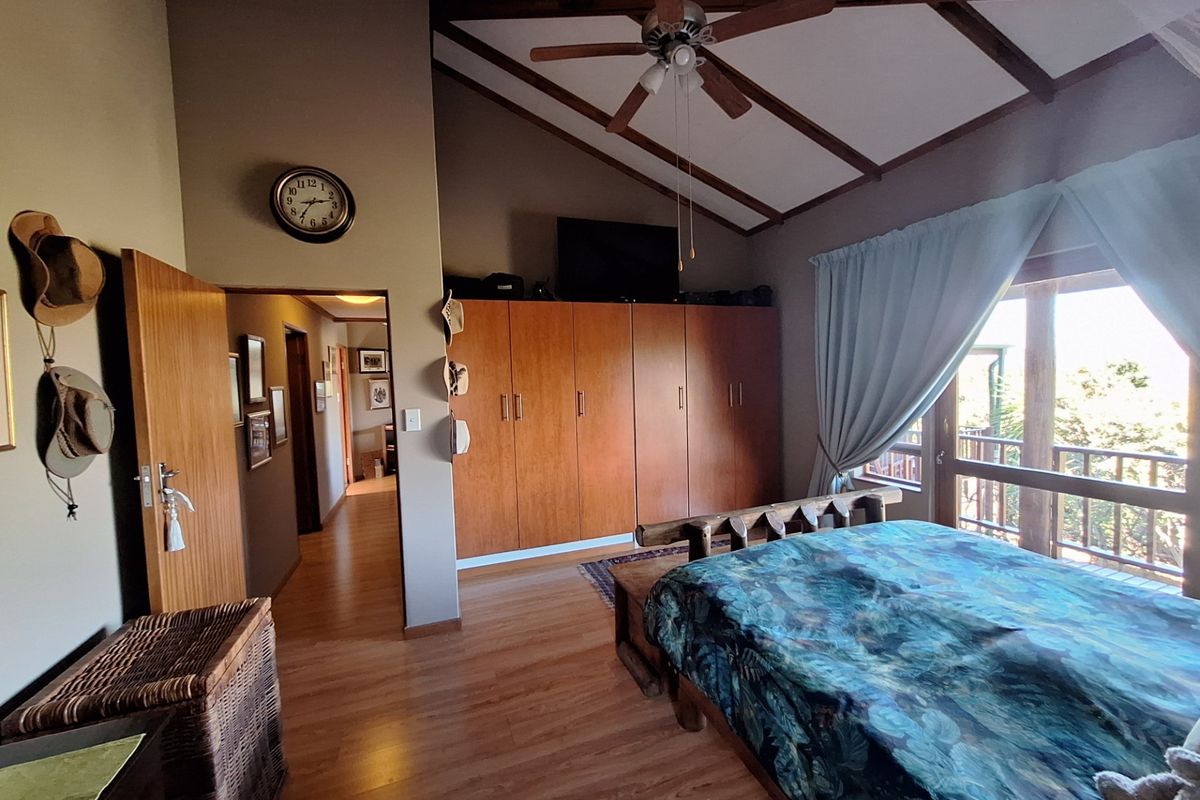 Spacious bedroom featuring vaulted ceilings with exposed timber beams, built-in wooden cabinetry, laminate flooring, and direct access to an outdoor balcony.