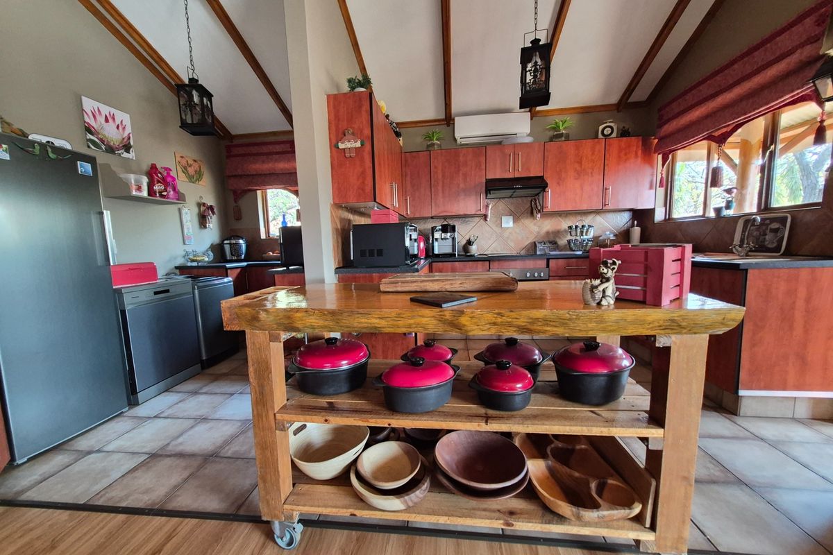 Spacious kitchen featuring warm-toned wooden cabinetry, tiled backsplash, exposed timber ceiling beams, and a central wooden island, offering a functional and rustic cooking space.