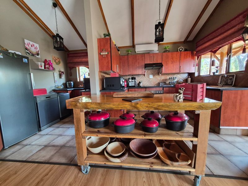 Spacious kitchen featuring warm-toned wooden cabinetry, tiled backsplash, exposed timber ceiling beams, and a central wooden island, offering a functional and rustic cooking space.