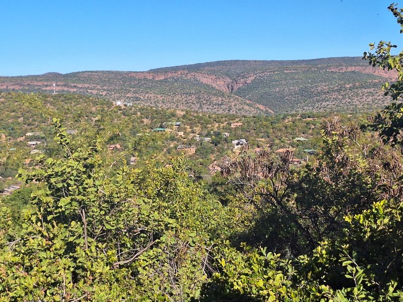 A scenic elevated view overlooking a natural landscape with distant hills and scattered residential properties nestled within the vegetation.