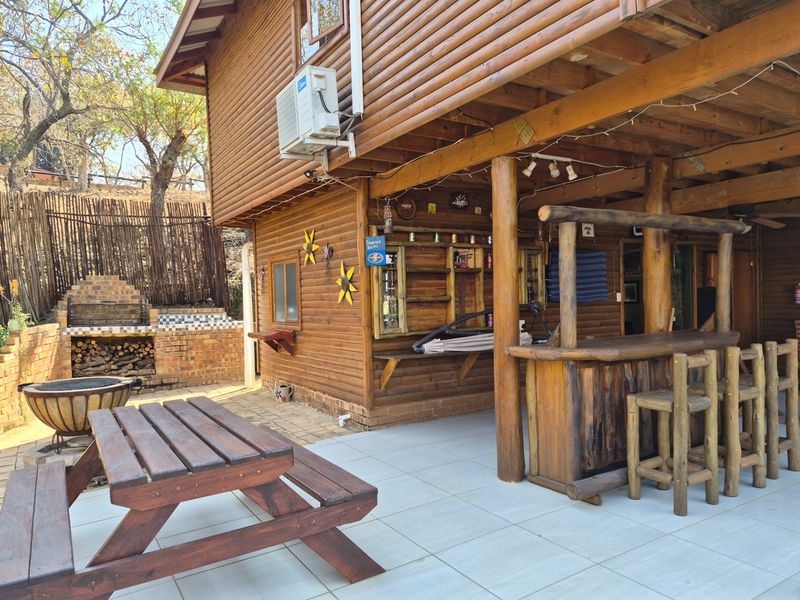 Covered outdoor patio area featuring a log cabin structure, built-in brick braai, and a rustic timber bar counter, ideal for outdoor entertaining.