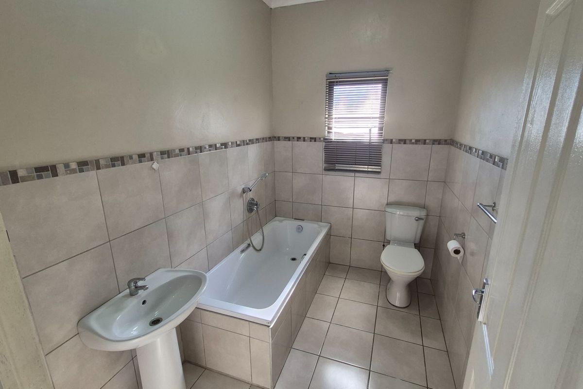 A functional bathroom featuring a pedestal basin, built-in bathtub, and toilet with neutral wall and floor tiling.