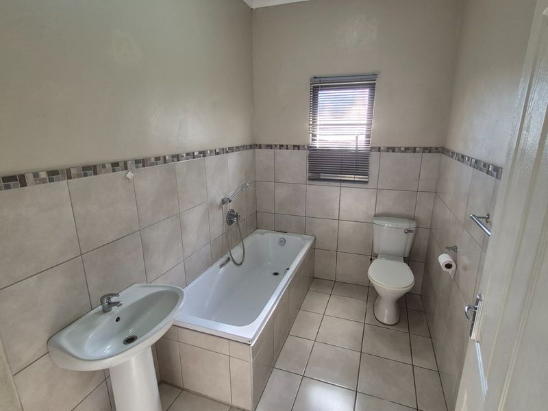 A functional bathroom featuring a pedestal basin, built-in bathtub, and toilet with neutral wall and floor tiling.
