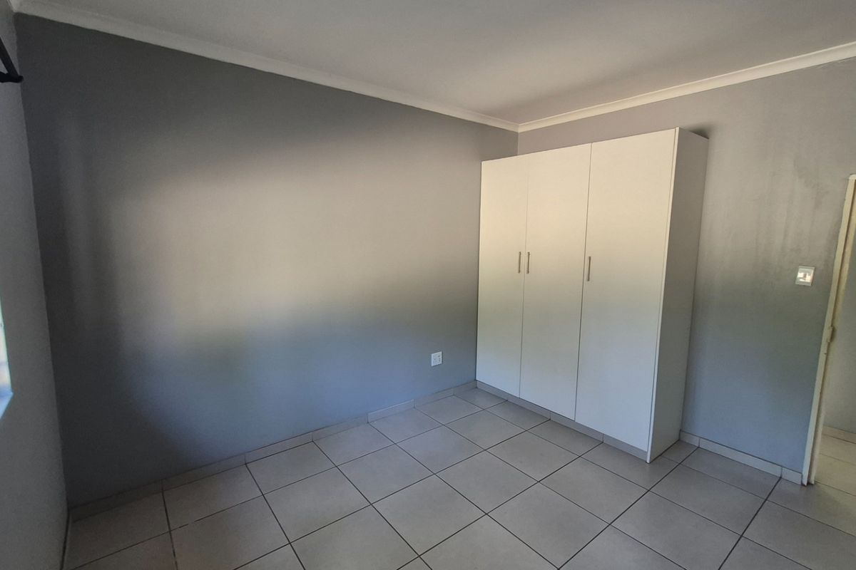 A clean, empty bedroom featuring neutral grey walls, tiled flooring, and a white built-in wardrobe.