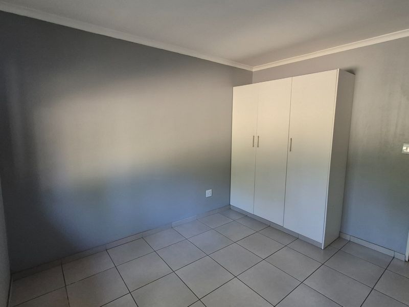 A clean, empty bedroom featuring neutral grey walls, tiled flooring, and a white built-in wardrobe.