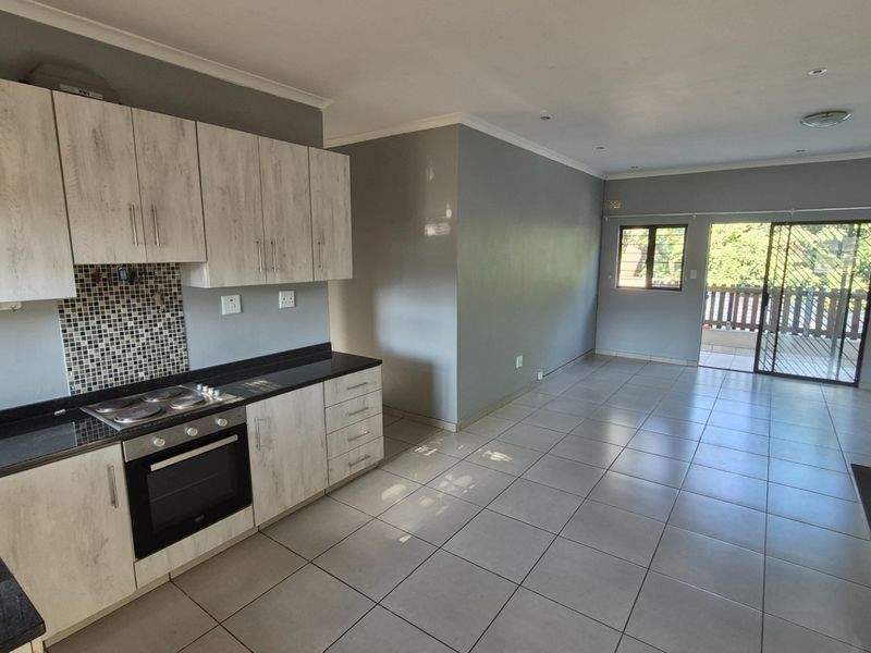 Spacious open-plan kitchen and living area featuring modern cabinetry, built-in appliances, tiled flooring, and direct access to an outdoor balcony.