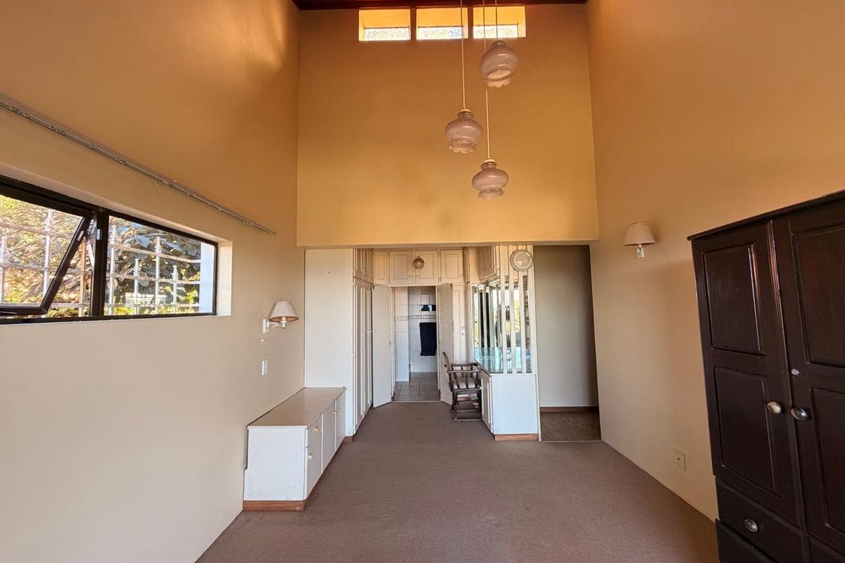 Spacious bedroom featuring high timber ceilings, built-in cupboards, a vanity area, and large windows with security bars.