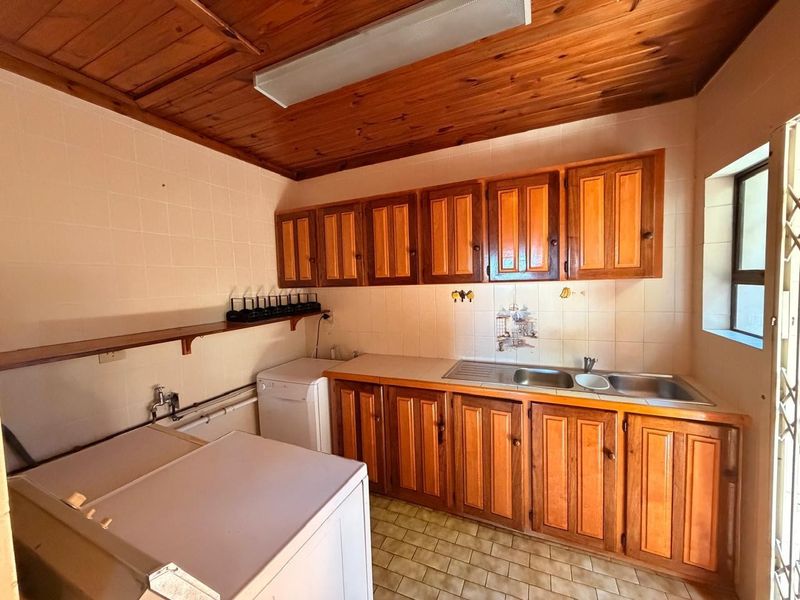 A dated kitchen featuring timber cabinetry, a double bowl stainless steel sink, tiled splashbacks, and a wooden ceiling with a fluorescent light fixture.
