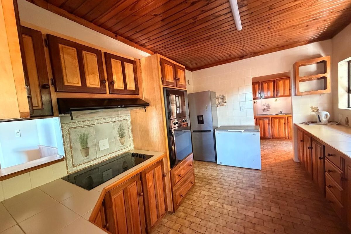 A spacious kitchen featuring extensive wooden cabinetry, tiled countertops, built-in oven, and a distinctive timber-clad ceiling, offering a functional layout with a separate scullery area.
