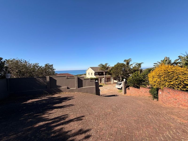 A view of the property entrance featuring a brick paved driveway, boundary walls, and a scenic coastal outlook.