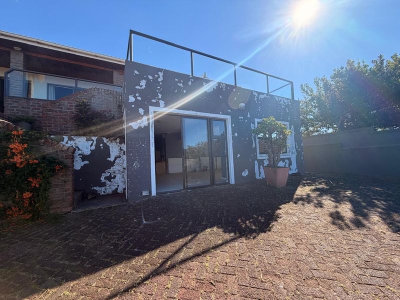 Rear exterior view of the property featuring a paved patio area, sliding glass doors, and an upper balcony with a metal railing.