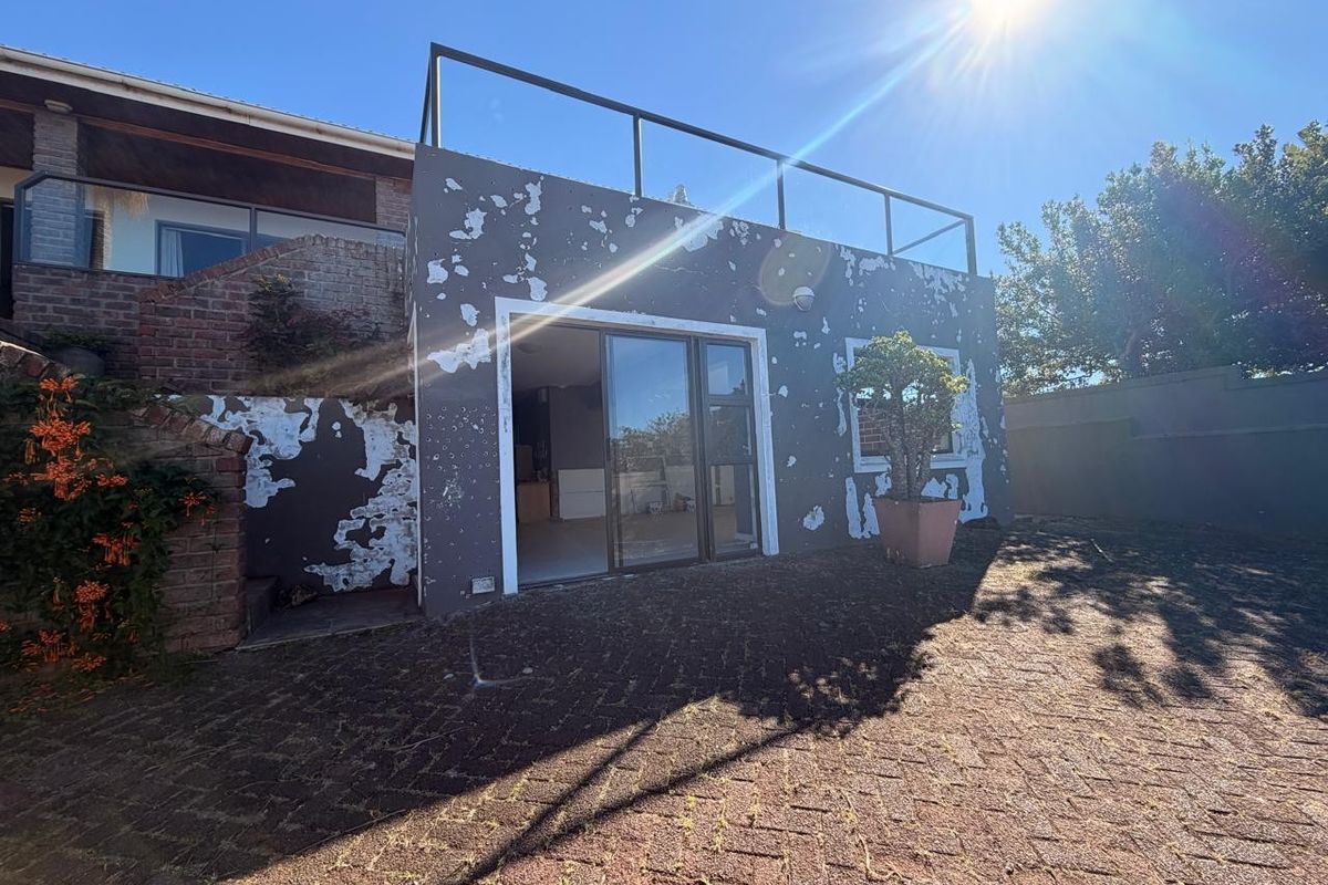 Rear exterior view of the property featuring a paved patio area, sliding glass doors, and an upper balcony with a metal railing.