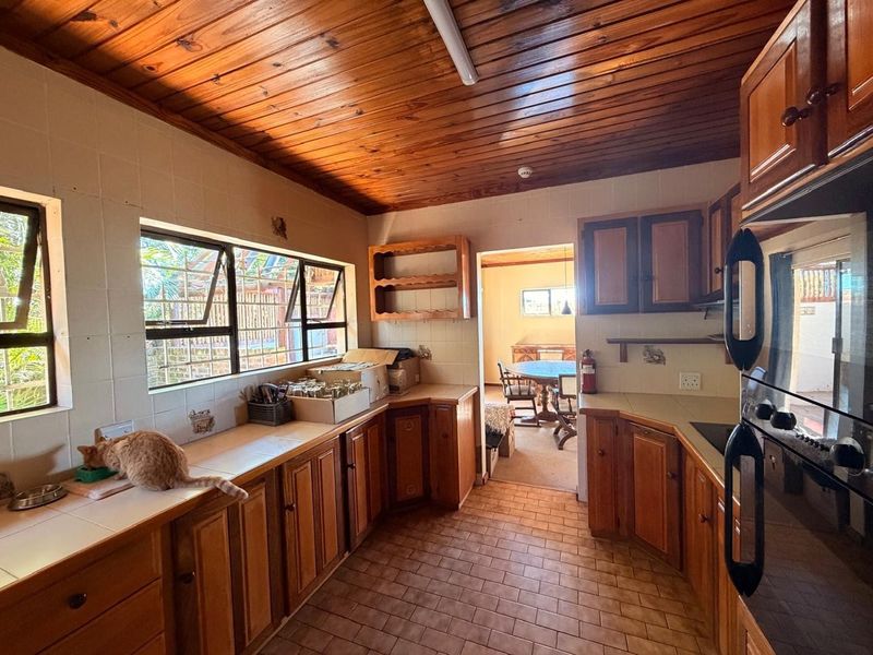 A dated kitchen featuring timber ceilings, tiled countertops, and wooden cabinetry, offering a functional layout with potential for modern renovation.