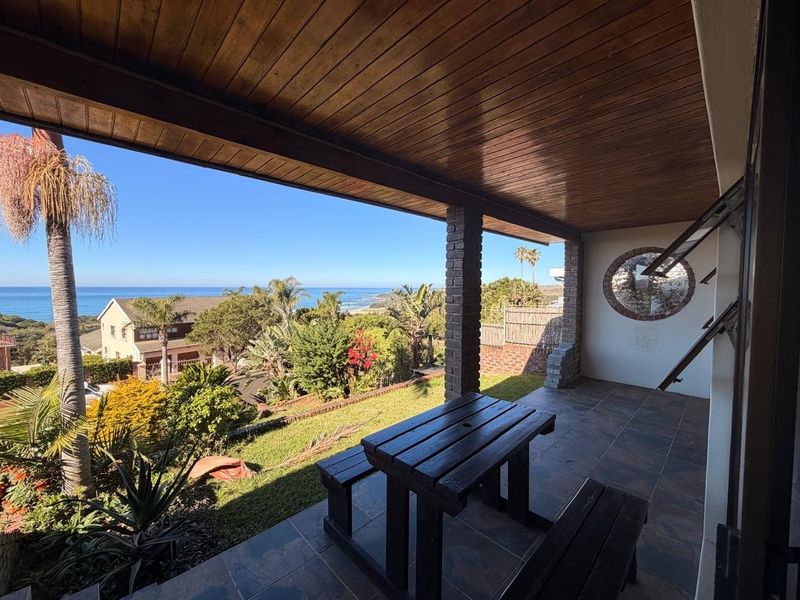 Covered patio featuring a timber ceiling, brick pillars, and tiled flooring, offering expansive views of the garden and ocean.