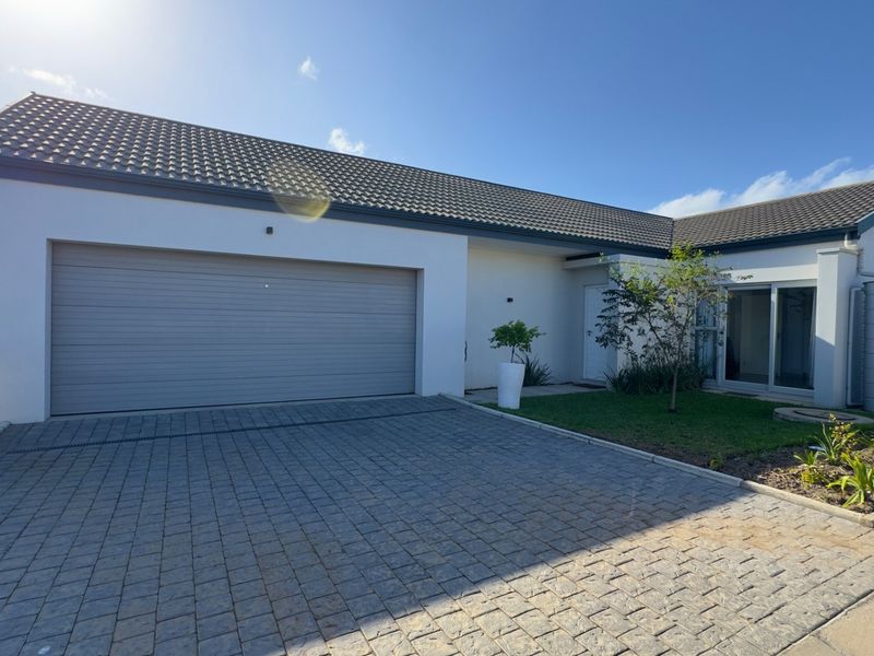 Front elevation of a modern house featuring a paved driveway, double garage, and a well-maintained garden area.