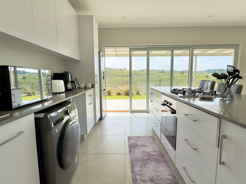 Modern kitchen featuring sleek white cabinetry, stone countertops, integrated appliances, and large sliding doors opening to a scenic outdoor view.