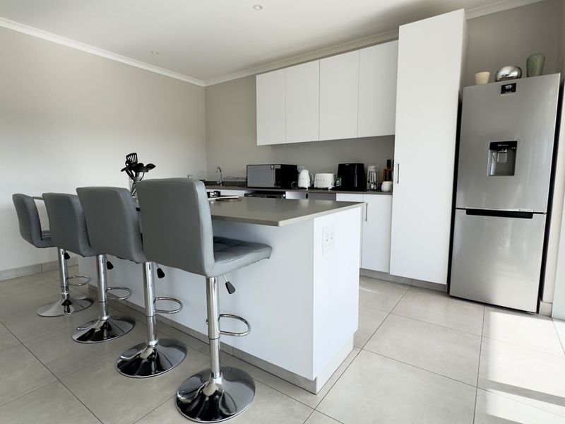Modern kitchen featuring a central island with stone countertops, sleek white cabinetry, and large format floor tiles, opening directly to an outdoor area.