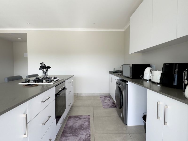 Modern kitchen featuring white cabinetry, stone countertops, a built-in oven, gas hob, and integrated laundry facilities in a clean, functional layout.