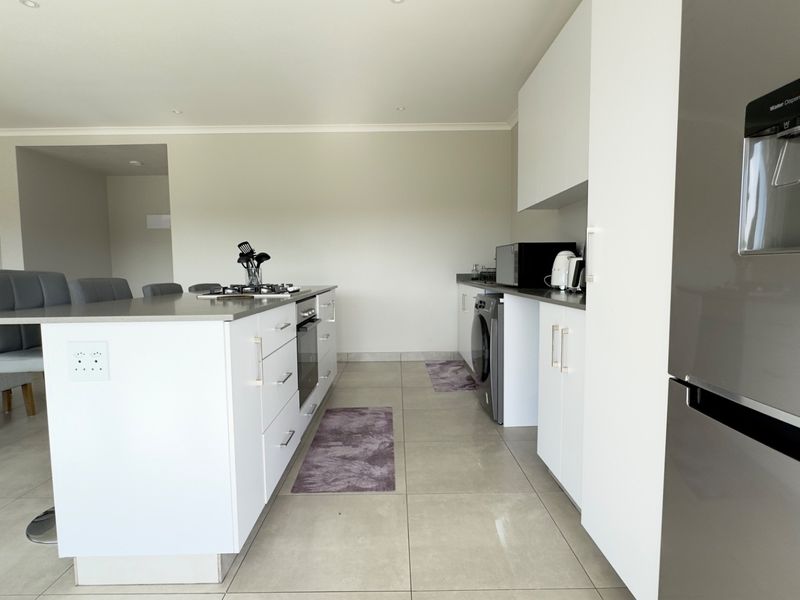 Modern kitchen featuring a central island with a built-in oven and gas hob, complemented by sleek white cabinetry and neutral tiled flooring.