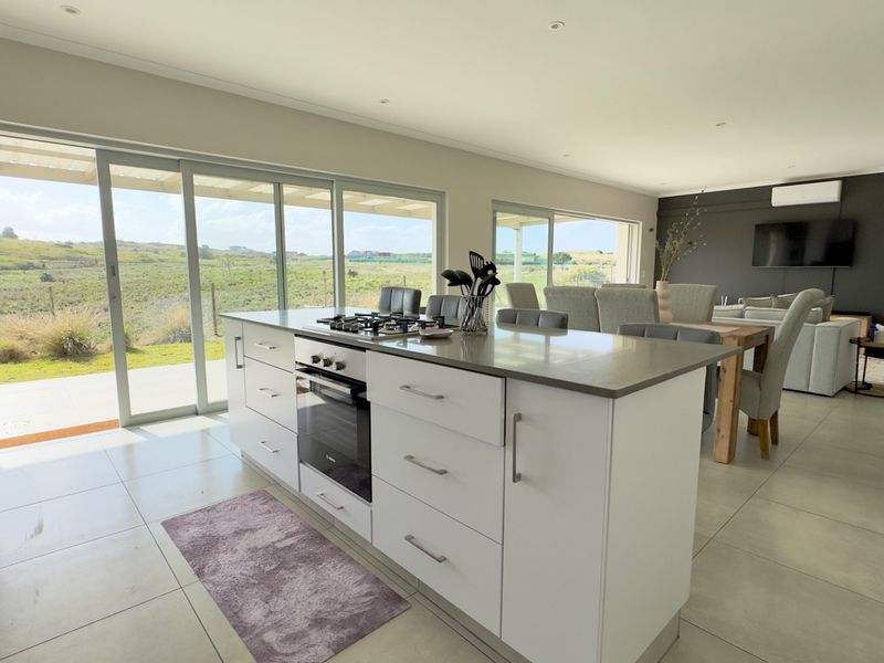 Spacious open-plan kitchen and living area featuring a central island with built-in appliances, sleek cabinetry, and large sliding doors opening to a scenic landscape.