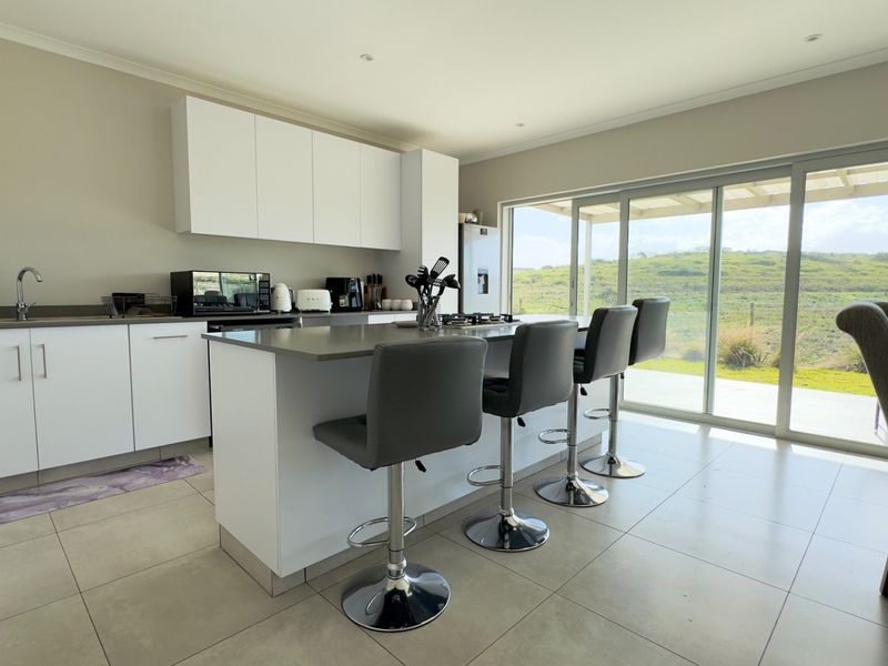 Modern open-plan kitchen featuring a central island with stone countertops, sleek white cabinetry, and large sliding doors opening to a scenic outdoor area.