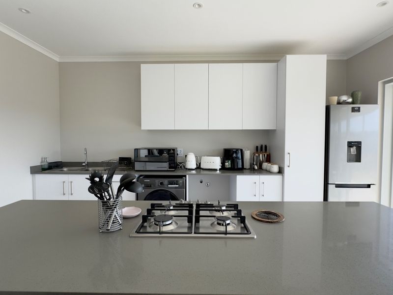 Modern kitchen featuring a central island with a gas cooktop, sleek white cabinetry, stone countertops, and integrated appliances with direct access to the outdoors.