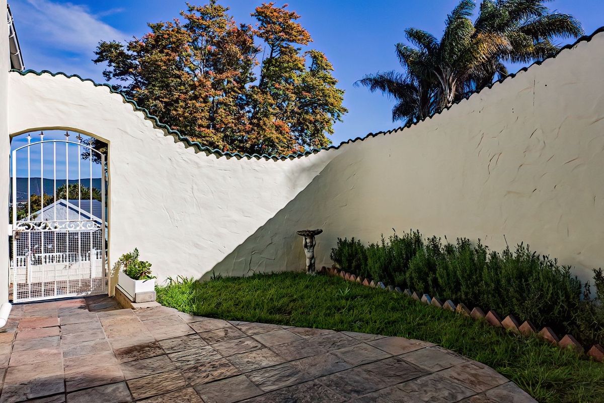 A private rear courtyard featuring a curved boundary wall, stone paving, and a decorative wrought iron gate leading to the exterior.