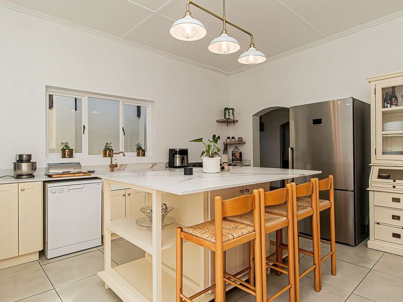 A well-maintained kitchen featuring a central island with stone countertops, ample built-in cabinetry, tiled flooring, and elegant pendant lighting.