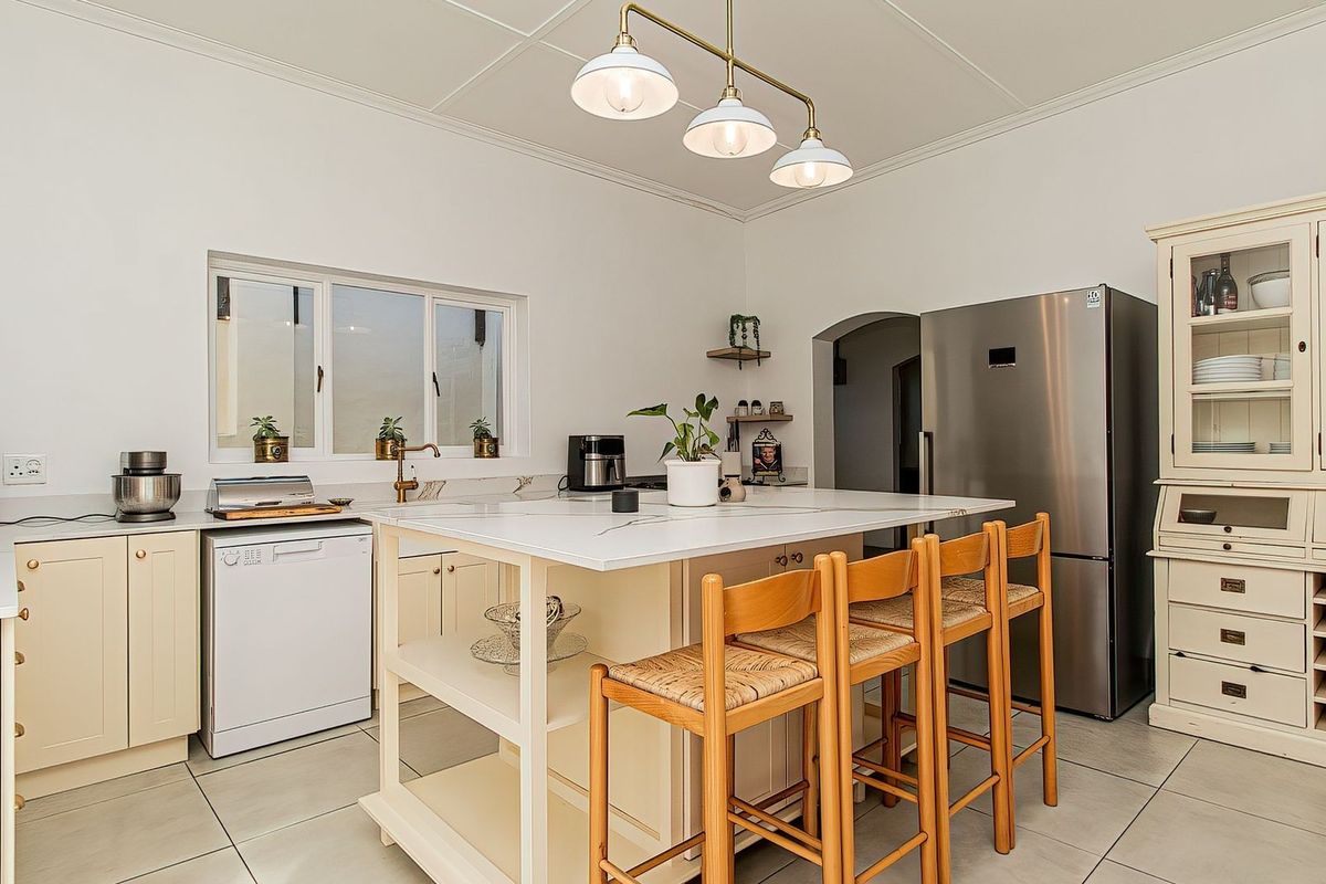 A well-maintained kitchen featuring a central island with stone countertops, ample built-in cabinetry, tiled flooring, and elegant pendant lighting.