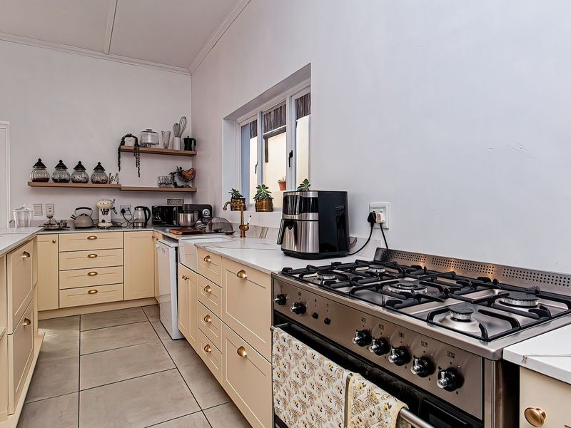A well-maintained kitchen featuring cream-colored cabinetry, stone countertops, a professional-style gas stove, and floating wall shelves.