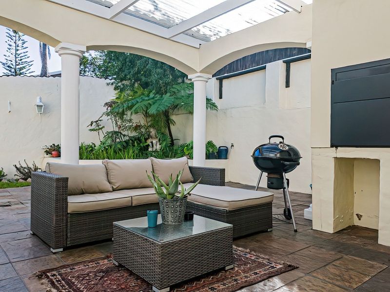 A covered outdoor patio featuring a built-in braai, classic columns, and paved flooring, providing a functional space for outdoor entertaining.