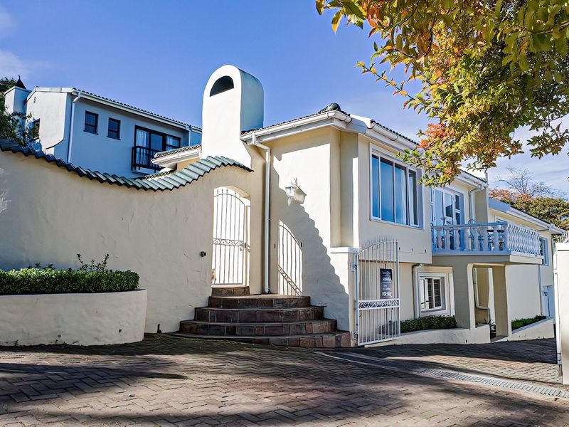 Front elevation of a multi-level residence featuring a paved driveway, secure gated entrance, stone steps, and a balcony with architectural detailing.
