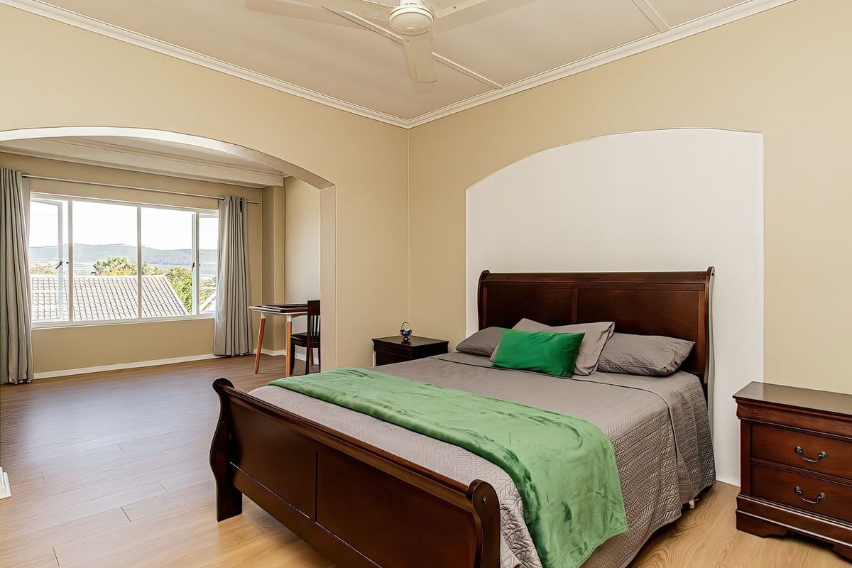 Spacious bedroom featuring light laminate flooring, a ceiling fan, and an adjoining sunlit alcove with large windows offering scenic views.