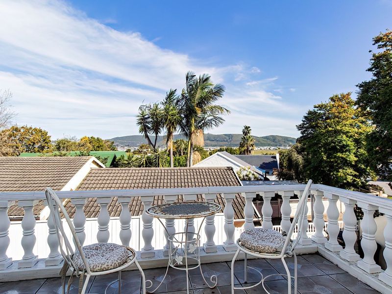 An elevated balcony featuring a classic balustrade and tiled flooring, offering scenic views of the surrounding neighborhood and distant mountains.