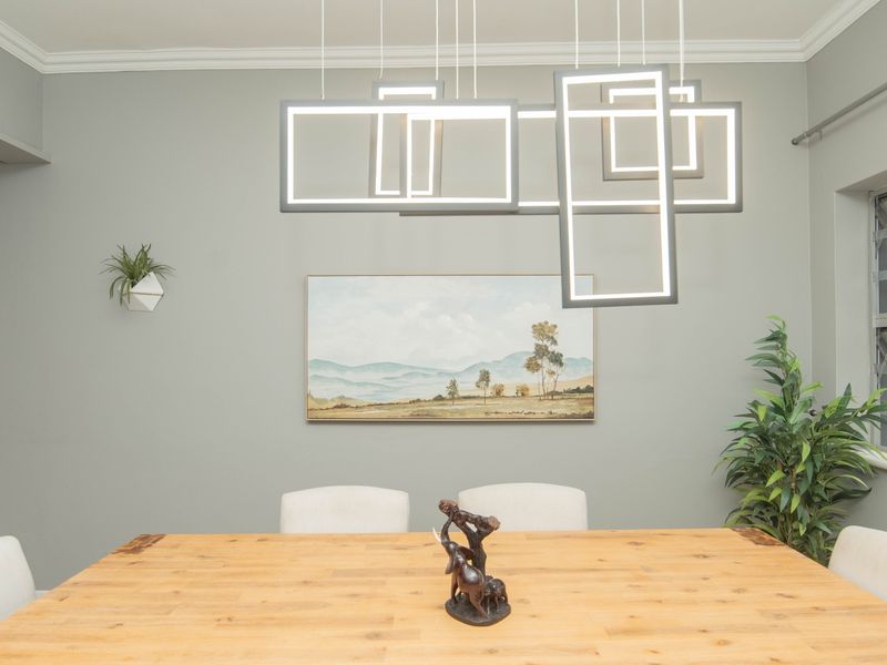 A well-lit dining room featuring a contemporary geometric pendant light fixture, crown molding, and neutral wall tones.