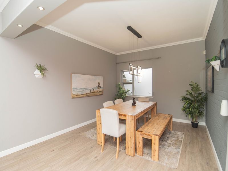 A well-maintained dining area featuring laminate flooring, recessed downlighting, and a textured painted brick feature wall.