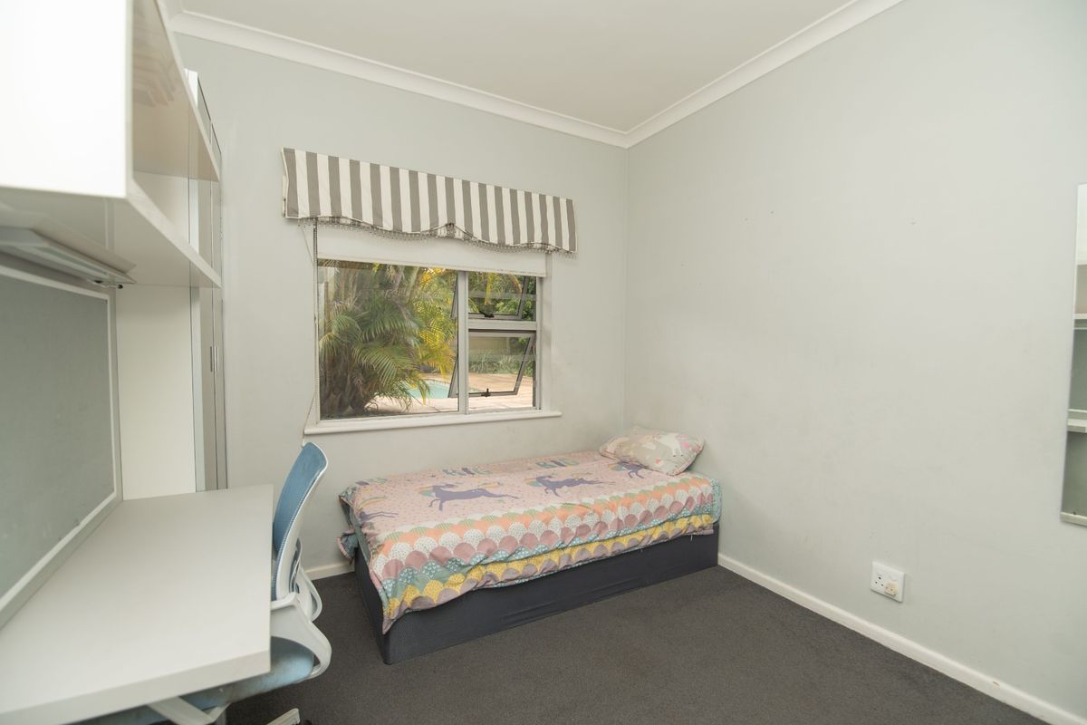 A functional bedroom featuring built-in desk and shelving units, carpeted flooring, and a window overlooking the garden area.
