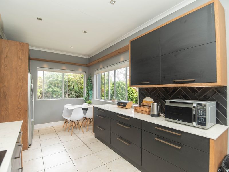 Modern kitchen featuring dark cabinetry, stone countertops, a stylish herringbone backsplash, and ample natural light from large windows overlooking the garden.