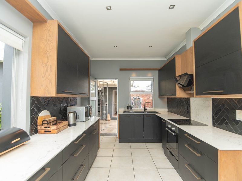 Modern galley-style kitchen featuring dark cabinetry, light stone countertops, a stylish herringbone backsplash, and integrated appliances with ample natural light.