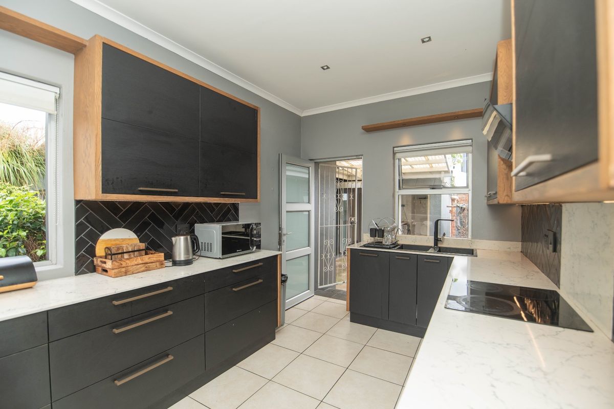 Modern kitchen featuring sleek black cabinetry, stone countertops, a herringbone tile backsplash, integrated hob, and high-quality finishes throughout.