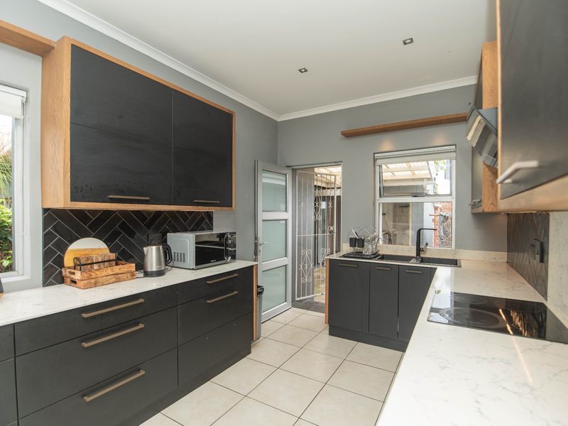 Modern kitchen featuring sleek black cabinetry, stone countertops, a herringbone tile backsplash, integrated hob, and high-quality finishes throughout.