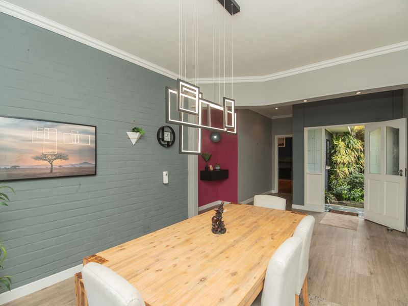 A well-maintained dining room featuring a modern pendant light, painted brick accent wall, and direct access to an outdoor area through a glass-paneled door.