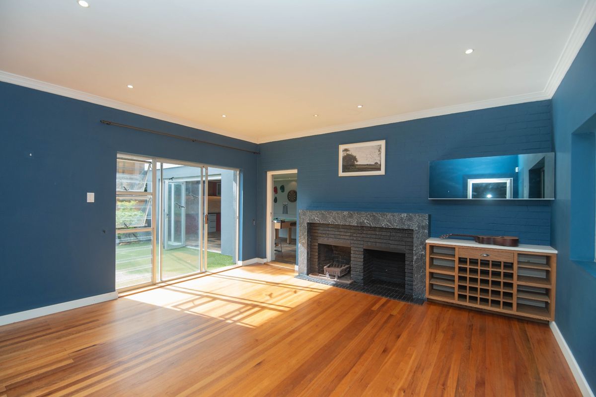 Spacious living room featuring polished hardwood floors, a striking blue brick wall, and a classic marble-surround fireplace with direct access to the outdoor area.