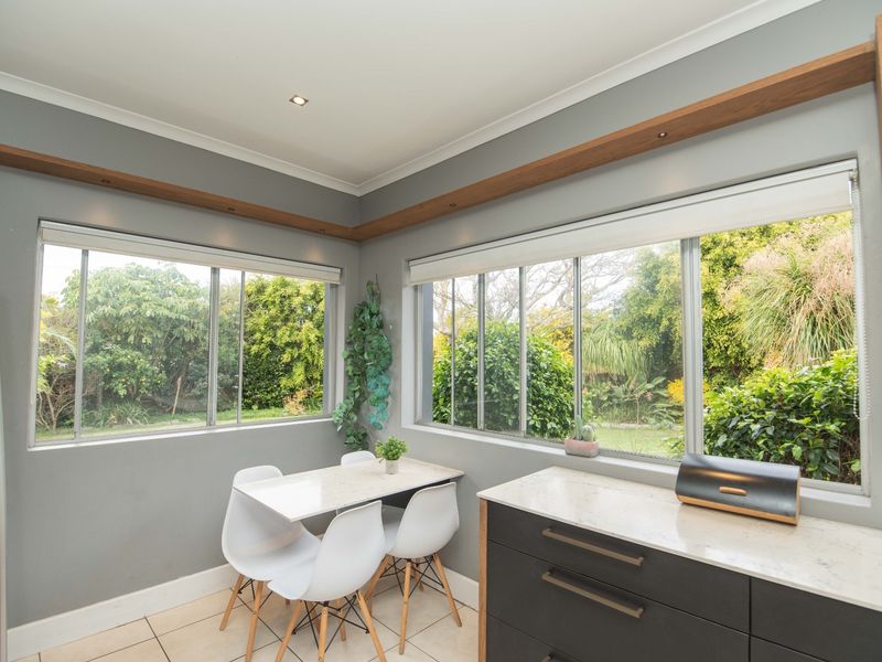 A bright kitchen breakfast nook featuring modern dark cabinetry, stone countertops, and large windows overlooking the garden.