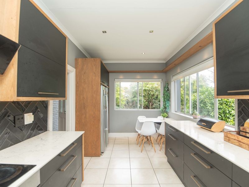 Modern kitchen featuring dark cabinetry, quartz countertops, herringbone tile backsplash, and large windows providing ample natural light and garden views.