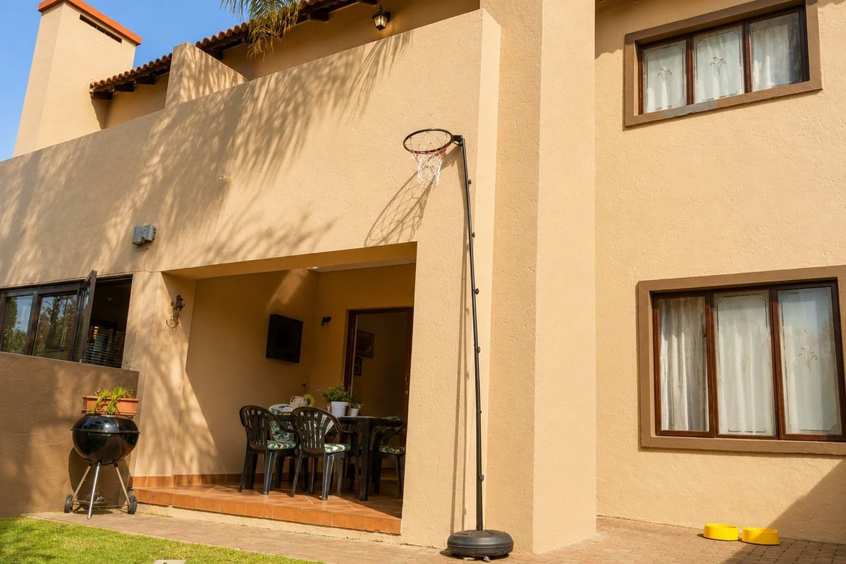 Rear view of the townhouse featuring a covered patio area, paved outdoor space, and traditional stucco facade with terracotta roof tiles.