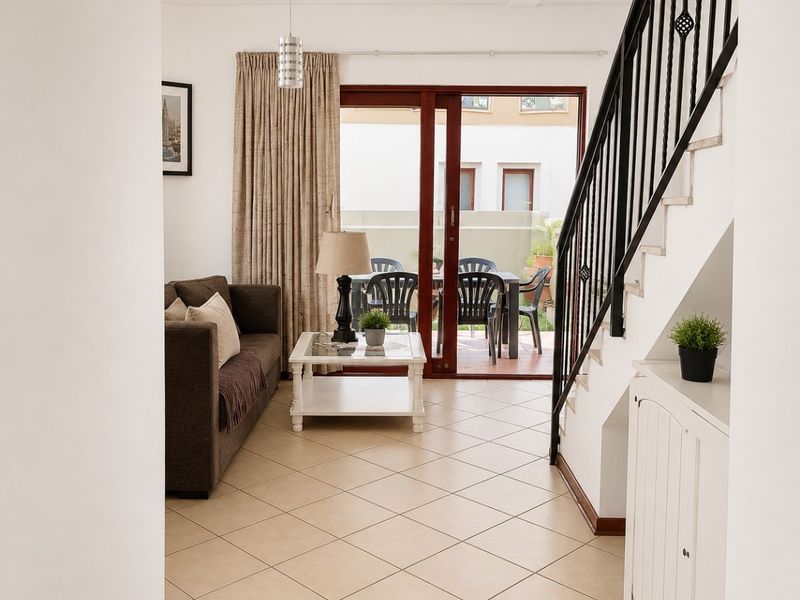 Bright living area featuring tiled flooring, a staircase with a metal balustrade, and sliding glass doors providing access to the patio.
