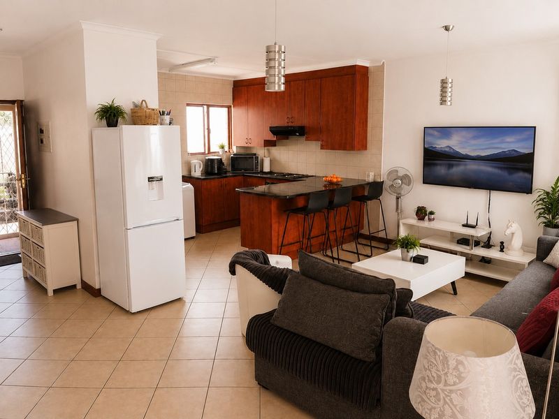 Open-plan living area featuring a kitchen with wood-finish cabinetry, granite countertops, and tiled flooring, seamlessly flowing into the lounge space.